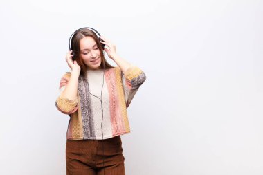 Genç sarışın güzel kız beyaz duvara karşı kulaklıkla müzik dinliyor.