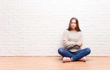 Genç sarışın güzel kız şüphe ediyor ya da düşünüyor, dudağını ısırıyor ve kendini güvende hissetmiyor ve gergin hissediyor, yerde otururken kopyalama alanı arıyor.