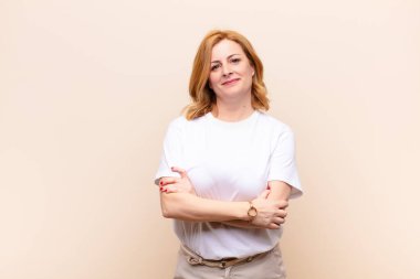 Orta yaşlı bir kadın mutlu, gururlu ve tatmin olmuş görünüyor. Kollarını kavuşturup gülümsüyor.