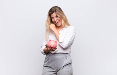 Genç, güzel Latin bir kadın mutlu, pozitif ve başarılı hissediyor, meydan okumayla karşılaştığında motive oluyor ya da beyaz duvara yaslanmış bir kumbarayla iyi sonuçları kutluyor.