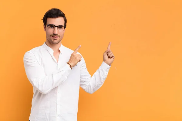 young handsome man smiling happily and pointing to side and upwards with both hands showing object in copy space