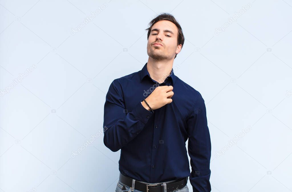 young handsome man looking arrogant, successful, positive and proud, pointing to self against blue wall