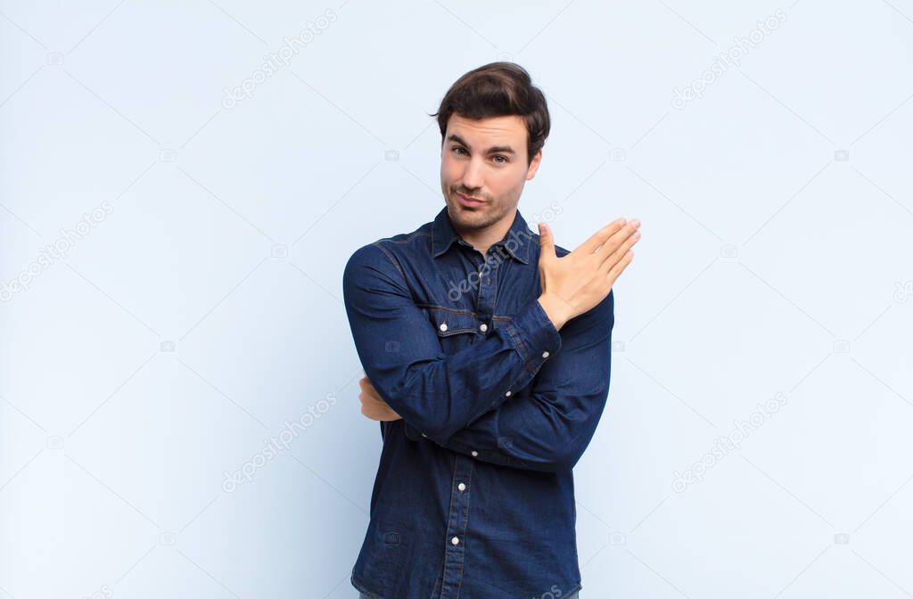 young handsome man feeling confused and clueless, wondering about a doubtful explanation or thought against blue wall