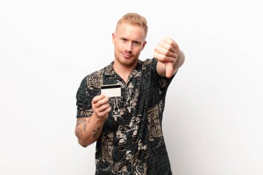 young blonde man feeling cross, angry, annoyed, disappointed or displeased, showing thumbs down with a serious look with a credit card clipart