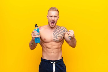 Genç sarışın güçlü adam sinirli, sinirli, sinirli bakışlar ve yumruklarla bağırıyor. Enerji içeceğine öfkeleniyor.