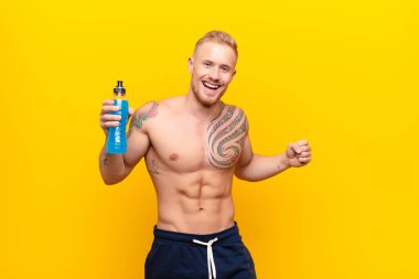 Genç sarışın güçlü adam gülümsüyor, tasasız ve mutlu hissediyor, dans ediyor ve müzik dinliyor, enerji içeceğiyle bir partide eğleniyor.