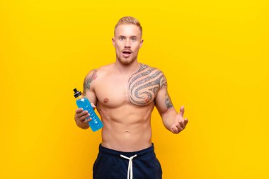 Genç sarışın güçlü adam şok olmuş ya da şaşırmış görünüyor, ağzı açık bakıyor ve enerji içeceğiyle 