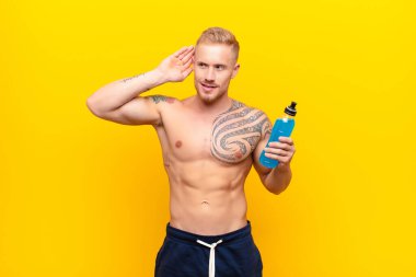 Genç sarışın güçlü adam gülümsüyor, tuhaf bir şekilde yan tarafa bakıyor, dedikoduları dinlemeye ya da enerji içeceğiyle bir sırrı duymaya çalışıyor.