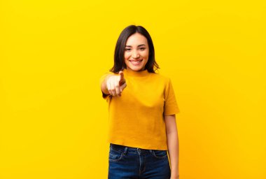 Genç, Latin, güzel bir kadın kameraya bakıyor. Tatmin olmuş, kendine güvenen, dost canlısı bir gülümsemeyle. Düz duvara karşı seni seçiyor.