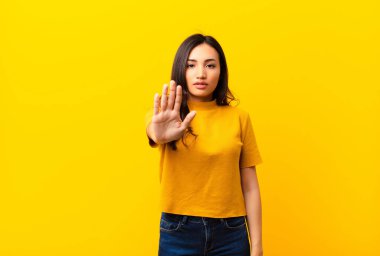 Genç Latin güzel kadın ciddi, sert, hoşnutsuz ve kızgın görünüyor. Avuç içini açıp düz duvara karşı jest yapıyor.