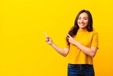 Genç Latin güzel kadın mutlu bir şekilde gülümsüyor ve iki eliyle yukarı ve yana doğru işaret ediyor fotokopi odasında düz duvara karşı nesne gösteriyor.