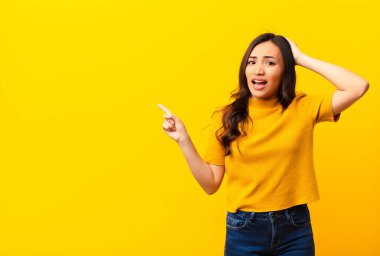 Genç Latin güzel kadın gülüyor, mutlu, pozitif ve şaşırmış görünüyor, düz duvara karşı yanal fotokopi alanını işaret eden harika bir fikrin farkına varıyor.