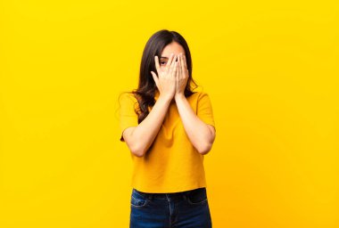 Genç, Latin, güzel bir kadın korkmuş ya da utanmış hissediyor. Gözleri yarı kapalı, elleri düz duvara yaslanmış bir şekilde dikizliyor ya da dikizliyor.