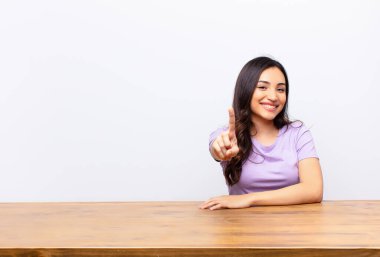 Genç Latin güzel kadın gururla gülümsüyor ve gururla bir numaralı pozu veriyor. Düz duvara karşı bir lider gibi hissediyor.