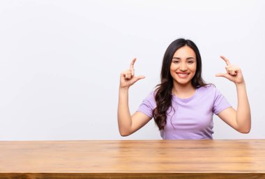 Genç, Latin, güzel bir kadın. İki eliyle gülücükler çiziyor. Olumlu ve mutlu görünüyor.