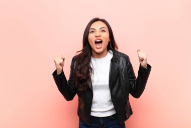 Genç, Latin, güzel bir kadın kızgın bir ifadeyle agresif bir şekilde bağırıyor ya da yumruklarıyla düz duvara karşı başarıyı kutluyor.