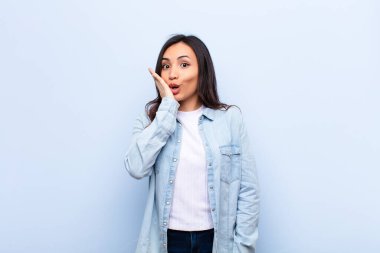 Genç, Latin, güzel bir kadın şok olmuş ve şaşkınlık içinde, ağzı sonuna kadar açık, yüz yüze inanmayarak duvara yaslanıyor.