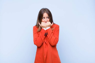 Genç, güzel İspanyol kadın endişeli, stresli ve korkmuş görünüyor. Tırnaklarını yiyor ve mavi duvara karşı yanal fotokopi çekmeye çalışıyor.