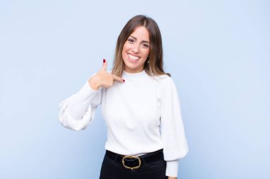 Genç, güzel İspanyol bir kadın mutlu, gururlu ve şaşırmış görünüyor. Neşeli bir şekilde kendini gösteriyor. Kendine güveniyor ve mavi duvara karşı kibirli.