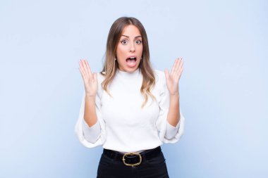 Genç ve güzel İspanyol kadın şok olmuş ve şaşkın bakıyor, mavi duvara karşı inanılmaz bir şey fark ettiğinde çenesi şaşkın ve şaşkın