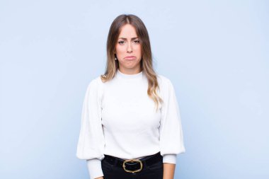 Genç, güzel, İspanyol bir kadın üzgün ve mızmızlanıyor. Mutsuz bir bakışı var. Mavi duvara karşı olumsuz ve hayal kırıklığına uğramış bir tavırla ağlıyor.