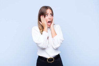 Genç, güzel İspanyol kadın mutlu, heyecanlı ve şaşırmış hissediyor, yüzünü mavi duvara dayayıp yan tarafa bakıyor.