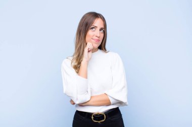 Genç ve güzel İspanyol kadın düşünüyor, kuşkulu ve şaşkın hissediyor, farklı seçenekleri var, mavi duvara karşı hangi kararı vereceğimi merak ediyor.