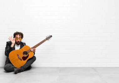 Genç müzisyen şok olmuş, şaşırmış ve şaşırmış hissediyor. Elinde gitar, rock 'n roll konseptiyle hayrete düşmüş, inanmayan bir bakış var.