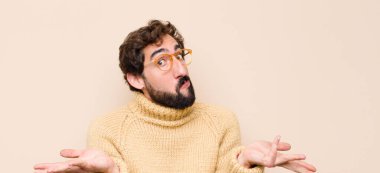 Genç havalı adam şaşkın ve şaşkın hissediyor, şüpheci, farklı seçenekleri tartıyor ya da seçiyor düz duvara karşı komik bir ifadeyle