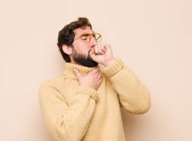 Genç, havalı bir adam boğaz ağrısı ve grip belirtileri ile hasta hissediyor, ağzı düz duvara dayalı öksürüyor.