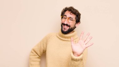 Genç havalı adam mutlu ve neşeyle gülümsüyor, el sallıyor, seni selamlıyor, ya da düz duvara karşı veda ediyor.