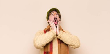 Genç havalı sakallı adam şok olmuş ve korkmuş hissediyor, ağzı açık ve elleri yanaklarında korkmuş görünüyor.