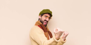 Genç havalı sakallı adam sinirli bir ifadeyle ya da yumruklarıyla başarıyı kutlarken agresif bir şekilde bağırıyor.