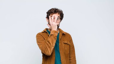 Genç yakışıklı adam şok olmuş, korkmuş ya da korkmuş görünüyor. Yüzü elle kaplanmış ve parmaklarının arasından düz duvara bakıyor.