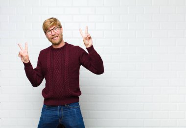 Genç sarışın adam gülümsüyor ve mutlu görünüyor, arkadaş canlısı ve memnun, işaret eden zafer ya da barış her iki eliyle iki eliyle de eski kiremitleri serpiştiriyor.