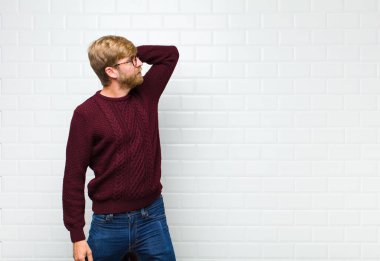 Genç sarışın adam düşünüyor ya da şüphe ediyor, kaşınıyor, kafası karışık ve şaşkın hissediyor, arkadan ya da arkadan bakıyor.