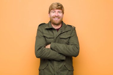 Genç, sarışın bir adam mutlu, gururlu ve memnun görünüyor. Kolları düz duvara çarpmış başarılı bir şekilde gülümsüyor.