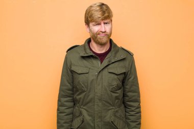 Genç sarışın adam kafası karışık ve kuşkulu, merak ediyor ya da düz duvara karşı karar vermeye çalışıyor.