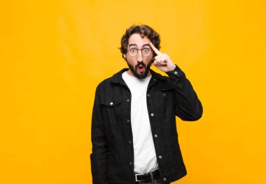 Genç çılgın yakışıklı adam şaşırmış, ağzı açık, şok olmuş turuncu duvara karşı yeni bir düşünce, fikir ya da konsept fark ediyor.