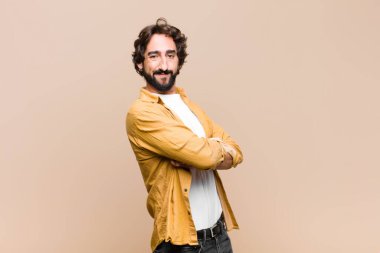 Genç, çılgın, havalı adam kameraya çapraz kollarıyla gülümsüyor ve mutlu, kendinden emin, tatmin olmuş bir yüz ifadesi var.