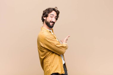 Genç çılgın havalı adam mutlu ve neşeli hissediyor, gülümsüyor ve seni selamlıyor, düz duvara karşı dostça bir jestle içeri davet ediyor.