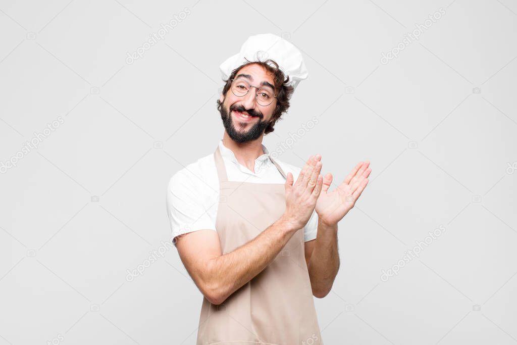 young crazy chef feeling happy and successful, smiling and clapping hands, saying congratulations with an applause against white wall