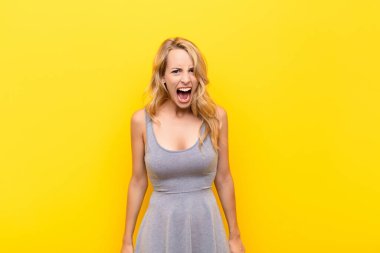 Genç sarışın kadın korkmuş ve şok olmuş hissediyor, ağzı açık turuncu duvara karşı şaşkınlık içinde.