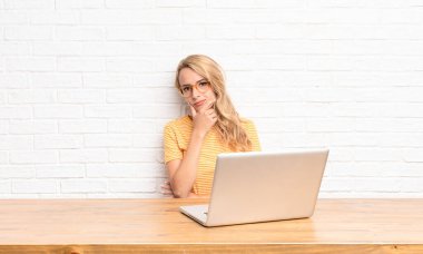 Genç sarışın kadın ciddi, düşünceli ve güvensiz görünüyor, bir kolu çapraz ve çene üzerinde, dizüstü bilgisayar kullanarak seçenekleri tartıyor.