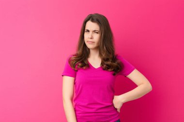 Genç ve güzel bir kadın kendini şaşkın ve kuşkulu hissediyor, merak ediyor ya da pembe duvara karşı karar vermeye çalışıyor.