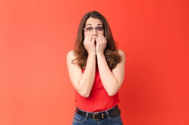 Genç, güzel bir kadın endişeli, gergin, stresli ve korkmuş görünüyor. Tırnaklarını yiyor ve kırmızı duvara karşı yanal fotokopi çekmeye çalışıyor.