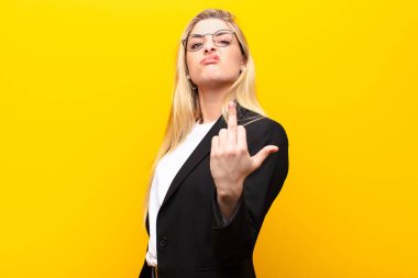 Genç, güzel sarışın kadın kızgın, sinirli, isyankar ve agresif orta parmağını sallayarak sarı duvara karşı savaşıyor.