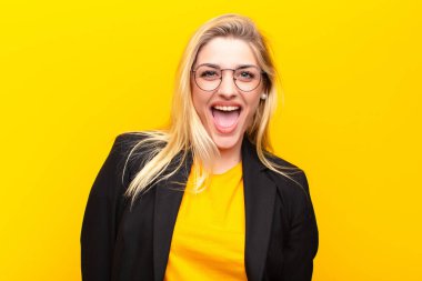 Genç ve güzel sarışın kadın mutlu ve hoş bir şekilde şaşırmış görünüyor, sarı duvara karşı büyüleyici ve şok edici bir ifadeyle heyecanlanıyor.