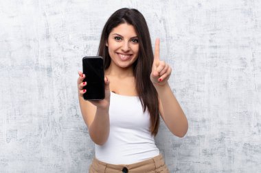 Genç ve güzel bir kadın akıllı telefonu grunge duvarına karşı kullanıyor.