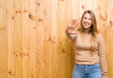 Genç sarışın kadın gülümsüyor ve arkadaş canlısı görünüyor. 5 ya da 5 numarayı gösteriyor. Eli önde, geriye doğru sayıyor.